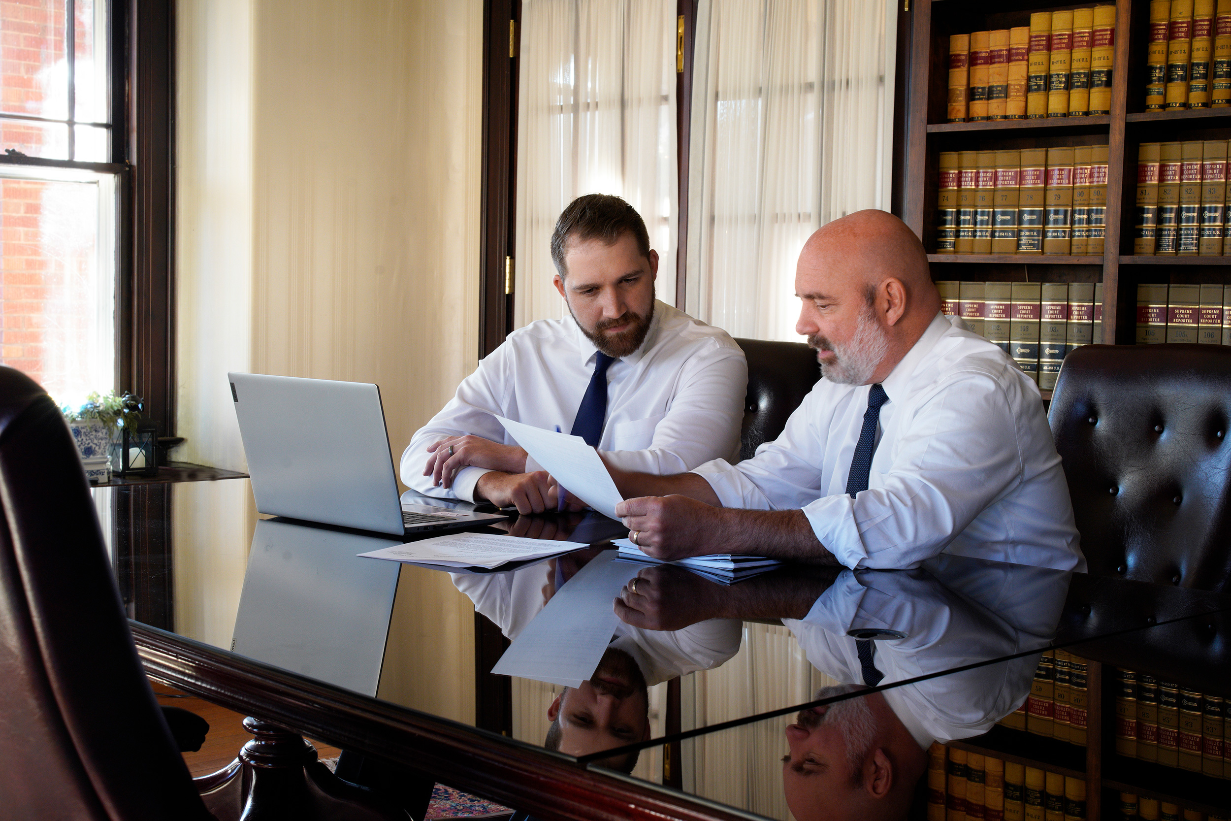 Shaffer & Shaffer employment lawyers Rich Walters and Ryan Walters (father and son), sit at a table at the law office looking over papers and a laptop. They help workers who experienced mistreatment on the job in West Virginia.