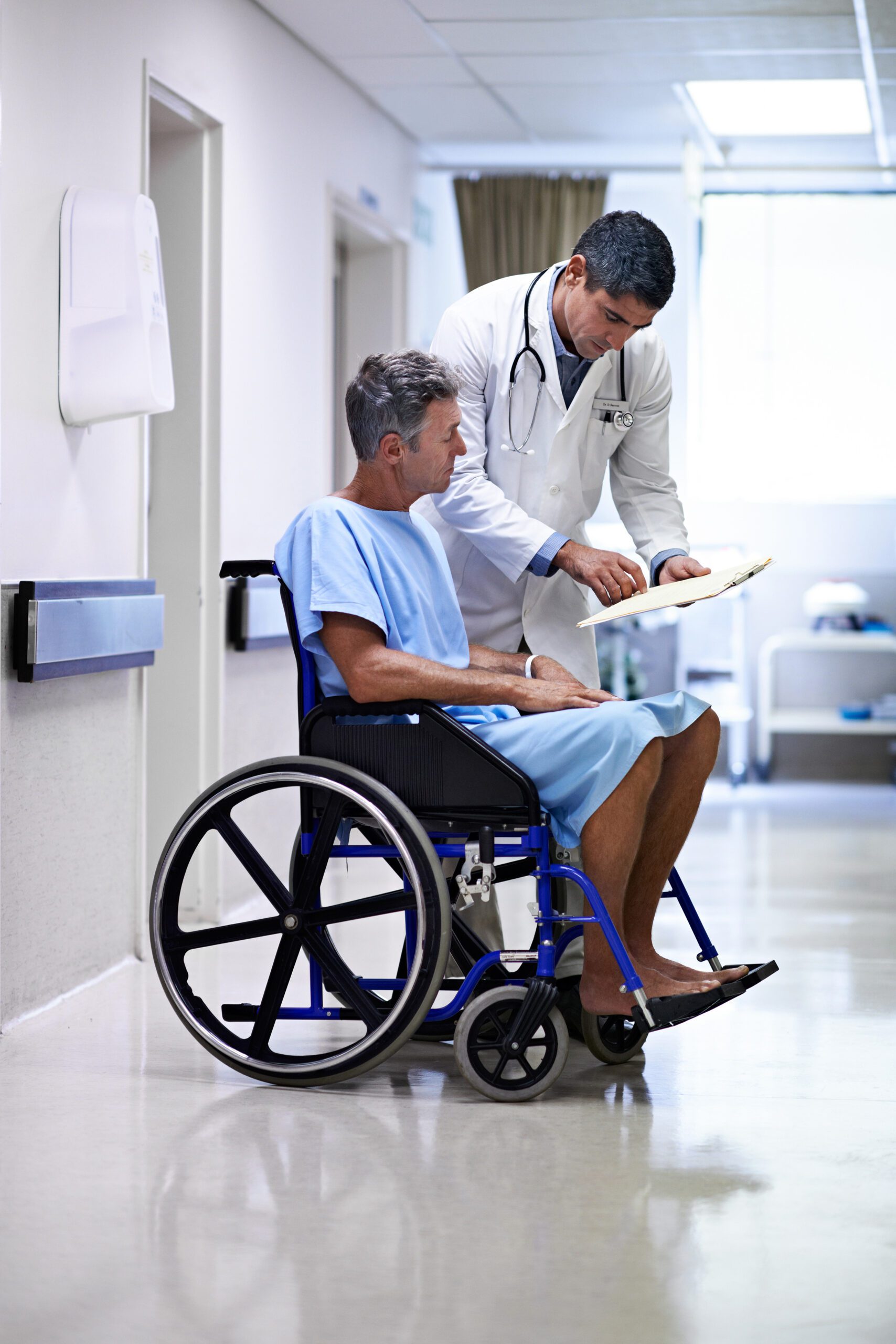 A doctor wearing a white coat and stethoscope talks to a man in a wheelchair. Multiple forms of harm can lead to a medical malpractice claim.