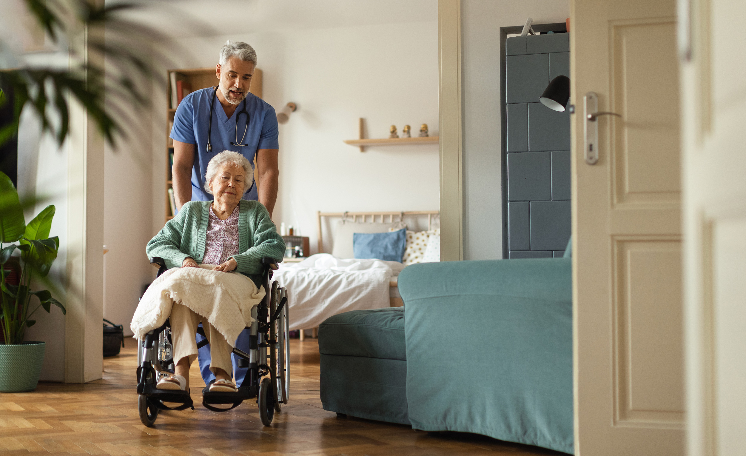 A health care worker wearing blue scrubs and a stethoscope pushes a woman in a wheelchair. Shaffer & Shaffer law firm has nursing home abuse lawyers in West Virginia.