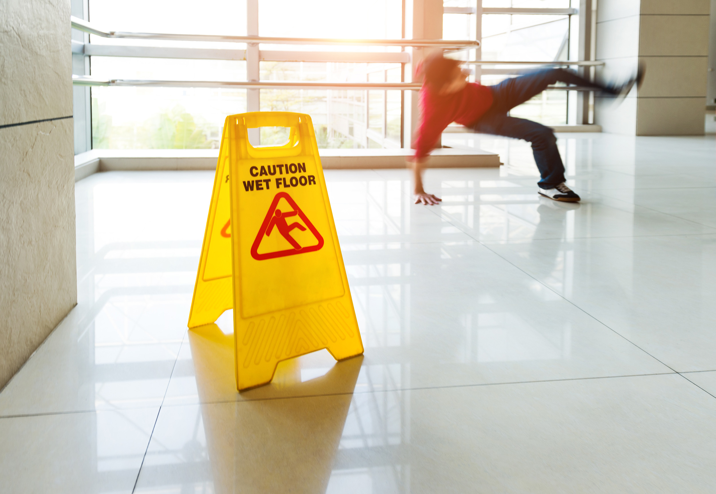 A man falls to the floor behind a "Caution: Wet Floor" sign. The West Virginia slip-and-fall lawyers at Shaffer & Shaffer help after injuries on unsafe property.