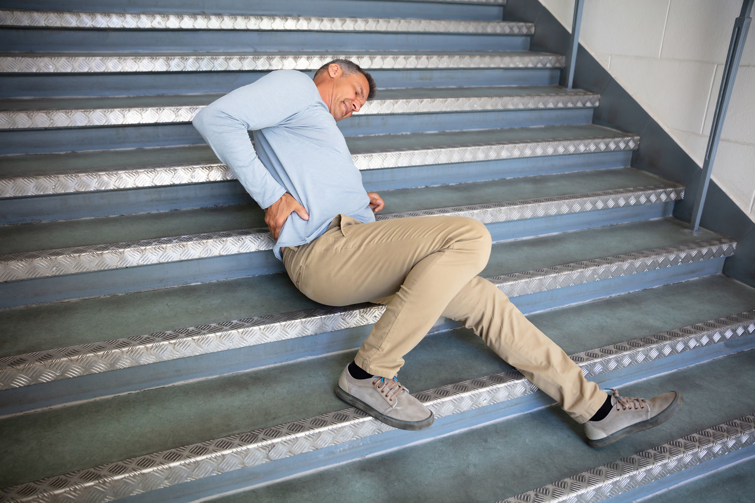 Lying on a set of stairs, a man who just fell holds his lower back. A slip-and-fall premises liability legal claim involves several steps.
