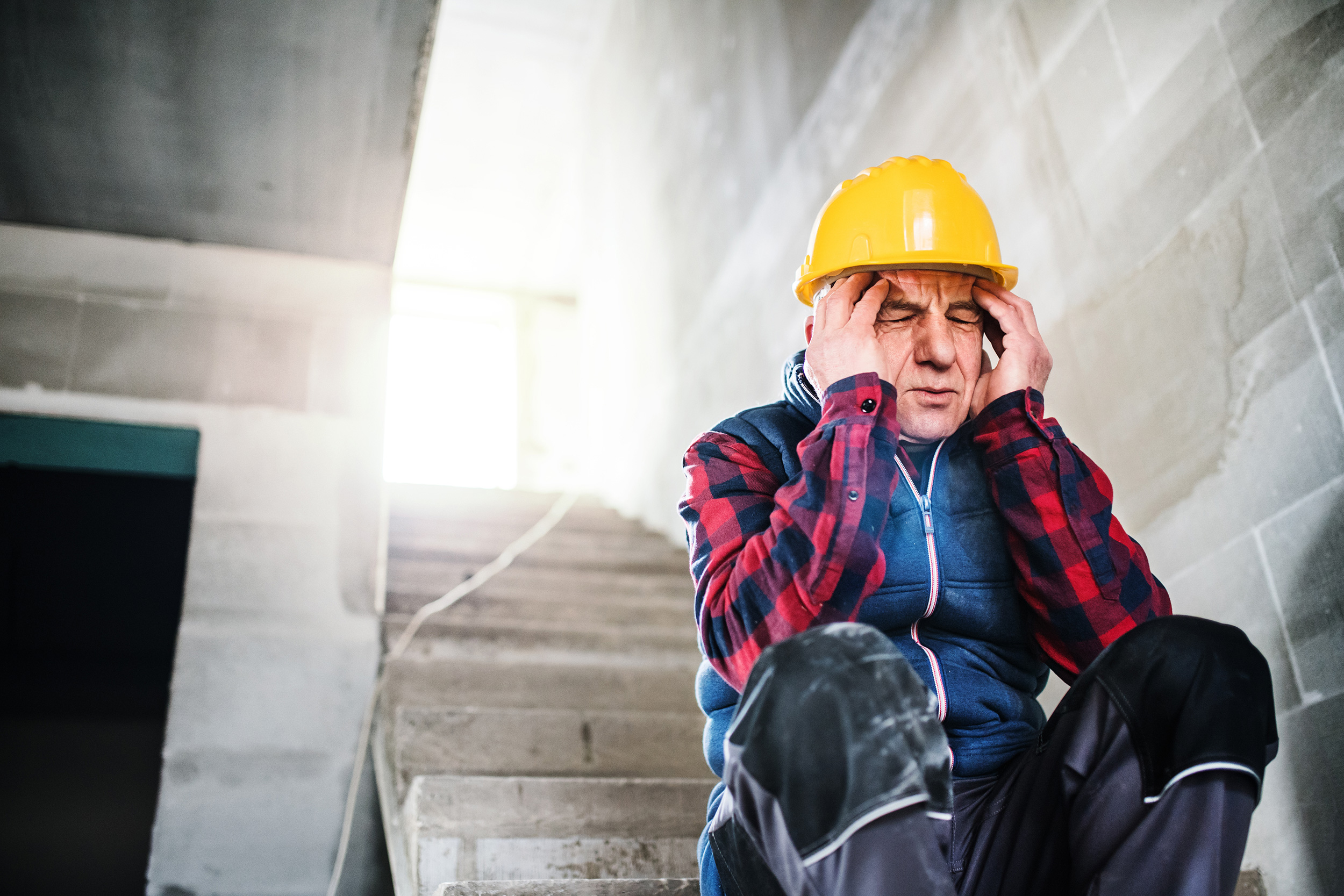 With his hard hat off, a man sits on the floor of a construction site and touches a cloth to a wound on his forehead. Injuries at work can lead to different kinds of compensation.