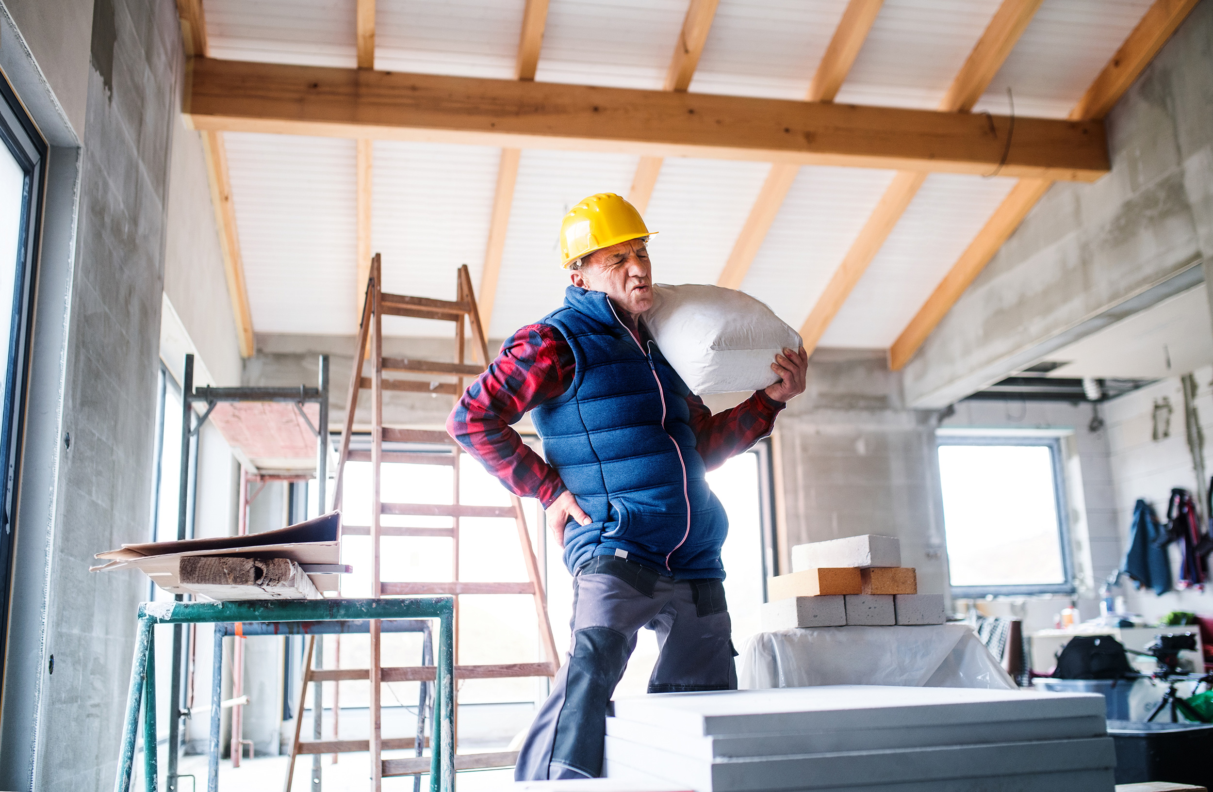 Picking up a heavy bag in a room under construction, a worker winces and puts his hand on his back. Any type of West Virginia worker can qualify for a claim under workers' injury law.
