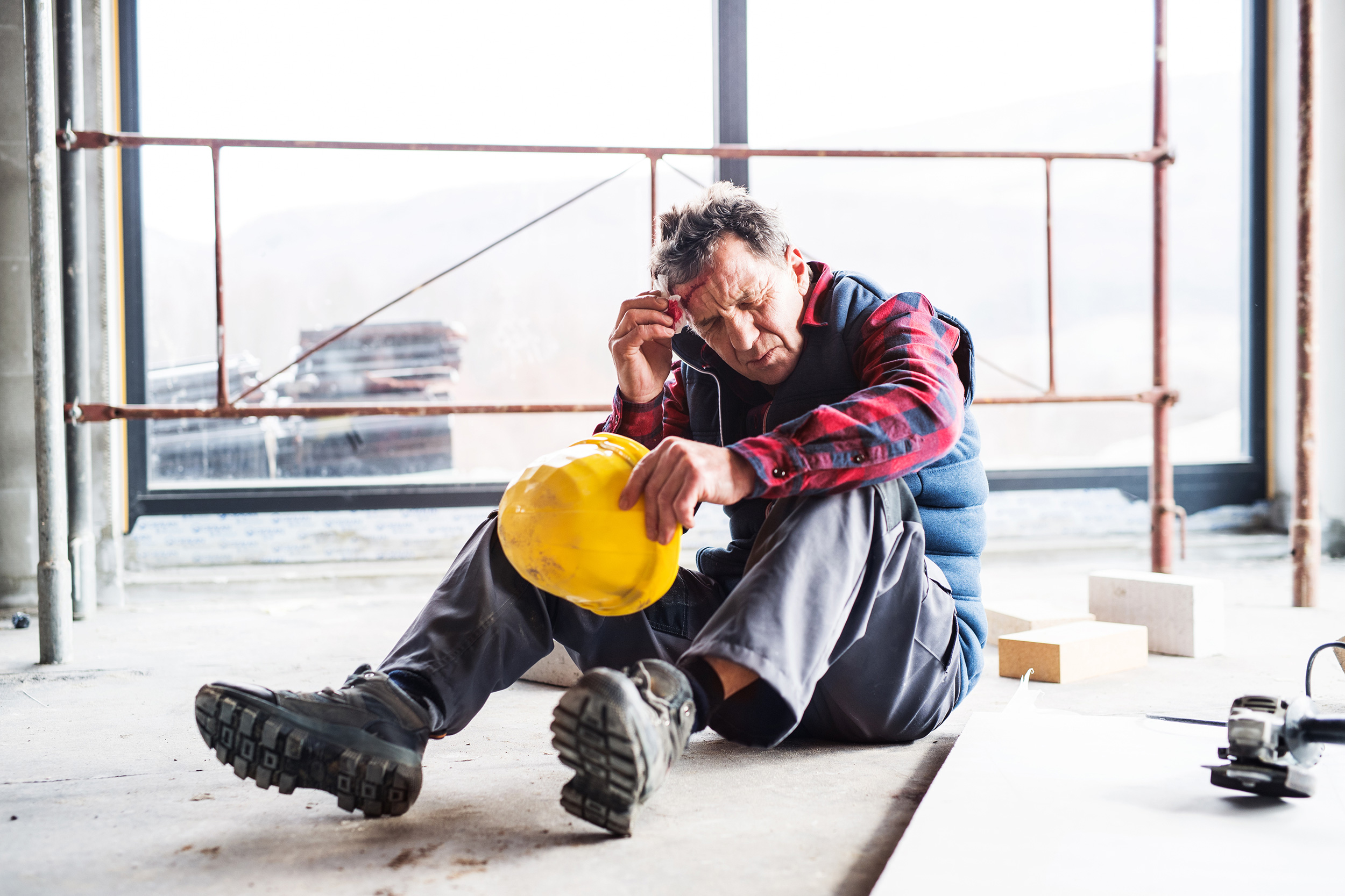 A man wearing a hard hat sits on the floor in a building under construction, closes his eyes and rubs is forehead. Shaffer & Shaffer workers' injury lawyers help people in West Virginia.